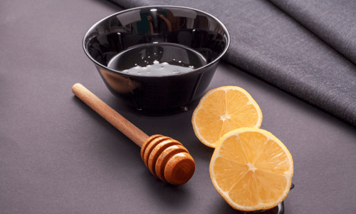 Close-up of lemon slices, a honey dipper, and a black bowl of honey.